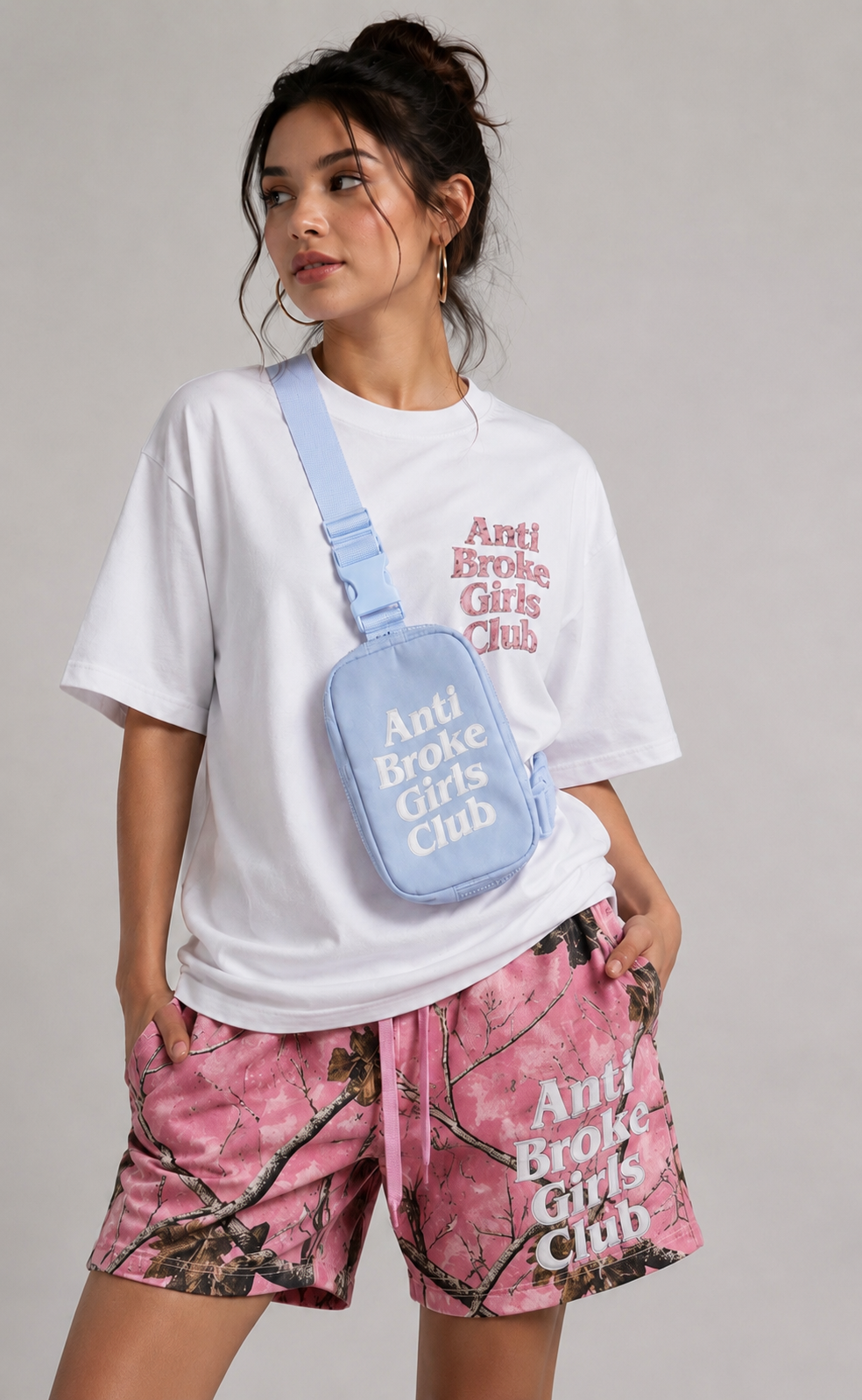 Person wearing 'Anti Broke Girls Club' t-shirt and shorts with a matching crossbody bag on a gray background