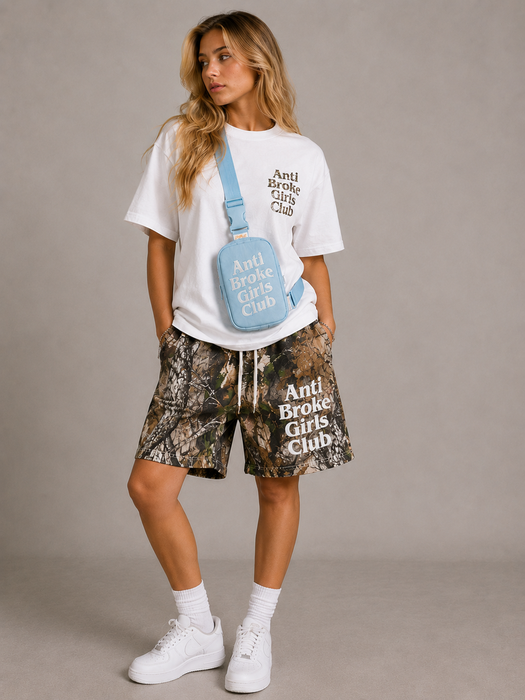 Person wearing a white t-shirt and camouflage shorts with 'Anti Broke Girls Club' text, holding a matching blue bag.